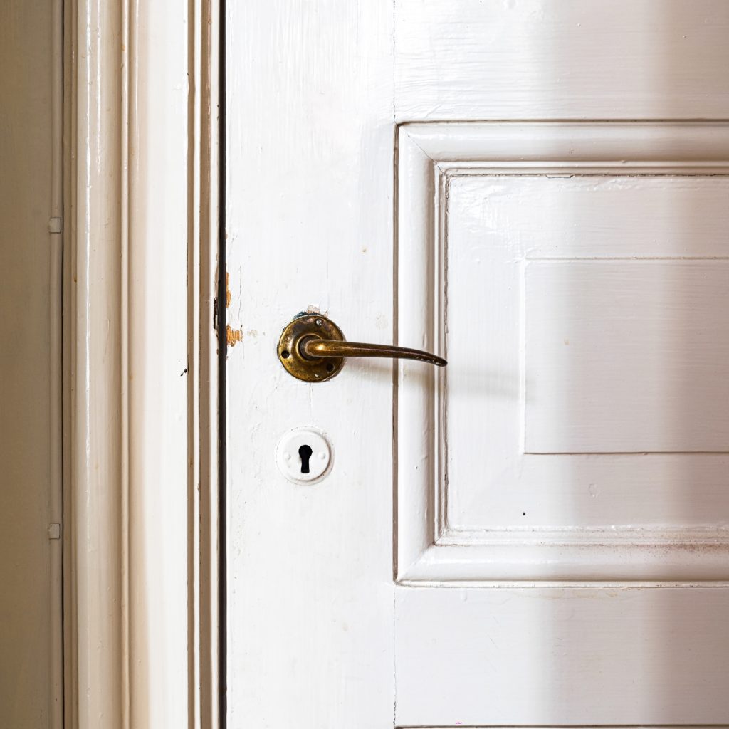 Detalles de una puerta de madera vintage blanca con pomo de estilo antiguo de bronce.
